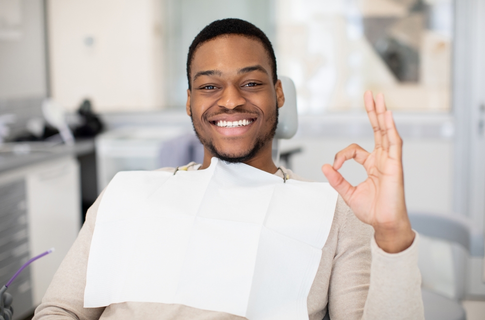 Happy Black Male Patient Sitting In Dentist Chair And Showing Ok Sign